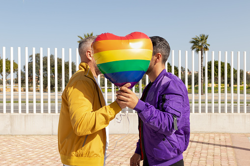 Gay couple behind a heart-shaped balloon in rainbow colors