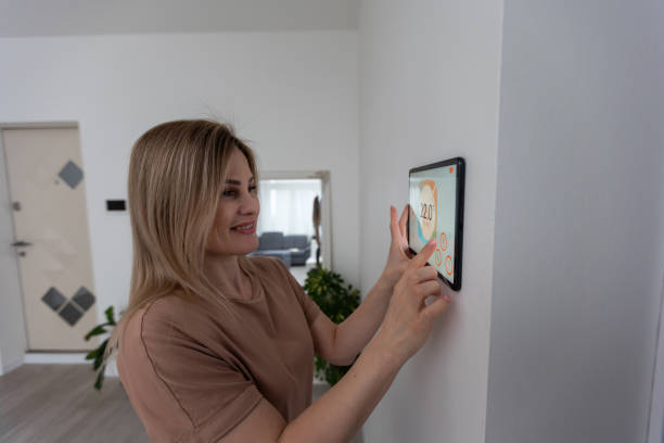 istock Woman controlling home with a digital touch screen panel installed on the wall in the living room 1475018669