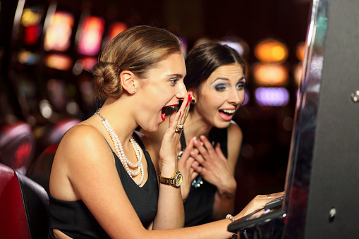 Two women sitting at Slot machine in Casion happy and excited for winning big.