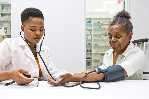 Female pharmacist measuring blood pressure of senior women in the pharmacy.