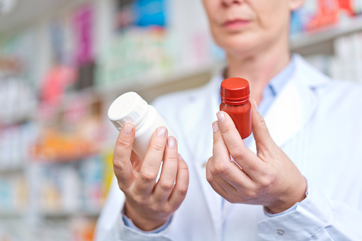Female pharmacists standing in front of medicine shelves and holding pill bottles. Close up of hands, unrecognizable person.