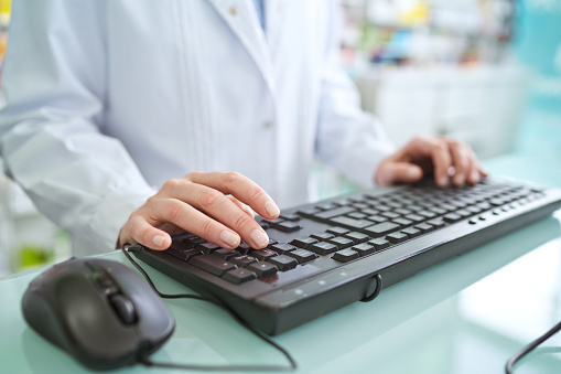 Male pharmacists using computer in pharmacy, close up of hands, unrecognizable person.