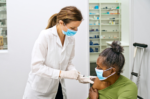 Pharmacist giving flu vaccine to a senior patient in pharmacy.