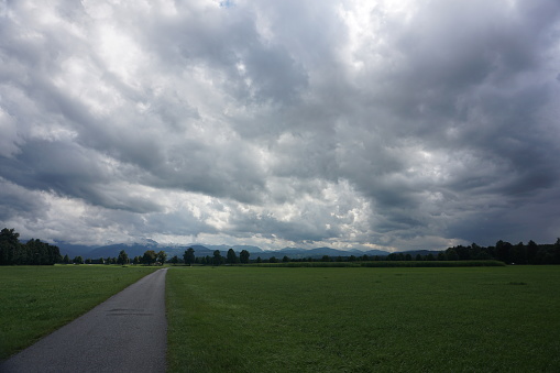 Dramatic sky over summer green fields and a walking path. Upper Bavaria in summer.