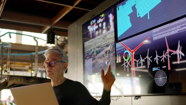 Mature man energy lecture A Stock photograph of a man conducting a seminar / lecture with the aid of a large screen. The screen is displaying data & designs concerning low carbon electricity production with solar panels & wind turbines. These are juxtaposed with images of conventional fossil fuel oil production. solar panel manufacturing stock pictures, royalty-free photos & images
