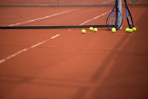 One single tennis ball between two white lines in the corner of a clay court with no people. Copy space,