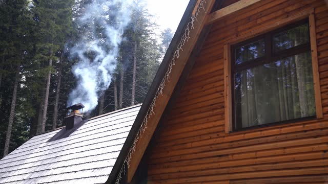 White smoke comes from the chimney of a wooden house in a coniferous forest