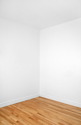 Empty corner of a renovated room with white walls and wooden floor.