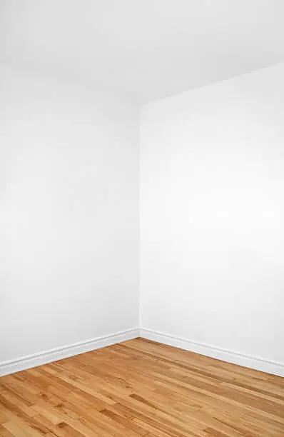 Empty corner of a renovated room with white walls and wooden floor.