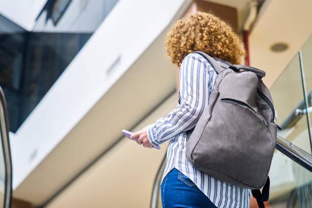 istock Adult woman holding smart phone while standing on escalator 1475030921