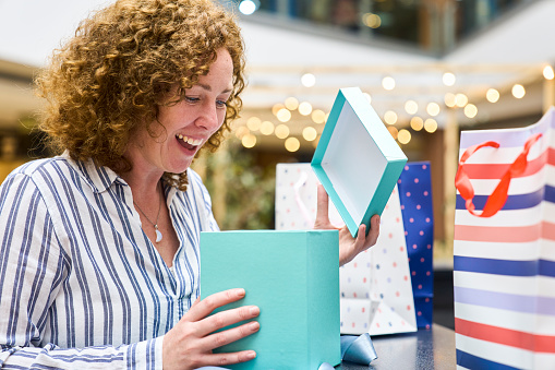 Side view of adult woman looking surprisely into gift box while standing in mall