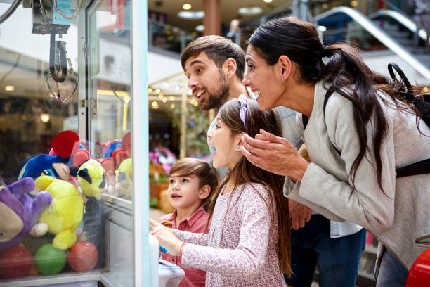 Little girl playing with toy grabbing machine while surrounded by family stock photo