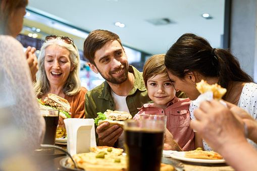 Portrait of cheerful family having fun during lunch time at shopping mall's food scourt during daytime