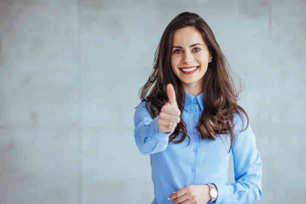 Young happy cheerful woman showing thumb up. Positive caucasian young girl woman showing thumb up looking at camera, checking for good quality recommendation isolated in grey background. Well done! Great job!