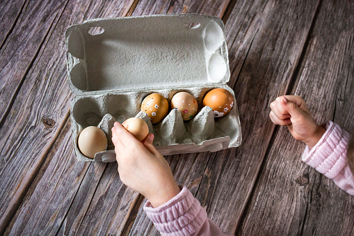 Overhead view on child's hands put Easter eggs in egg carton on wooden table