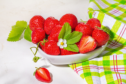 Strawberries in white porcelain bowl on a table. Bowl filled with juicy fresh ripe red strawberries. Selective focus