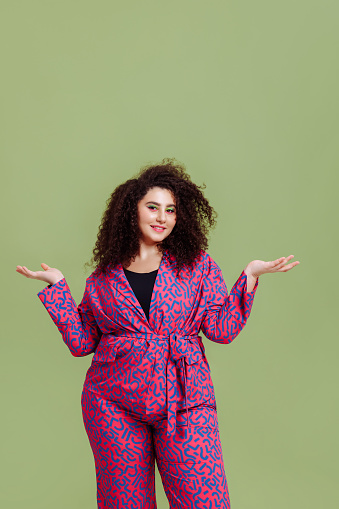 A young woman with a large figure in a bright suit depicts scales with her hands. Plus size model with afro hair. Weighs the pros and cons.