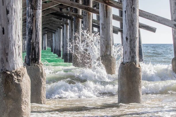 A beautiful view of the waves crashing against the pier from underneath the Newport Beach Pier in California.