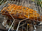 Close-up image of smoking portable, charcoal barbecue in garden, Red snapper being cooked outdoors in a metal grill basket, tikka paste marinated fish, lemon slice garnish, focus on foreground