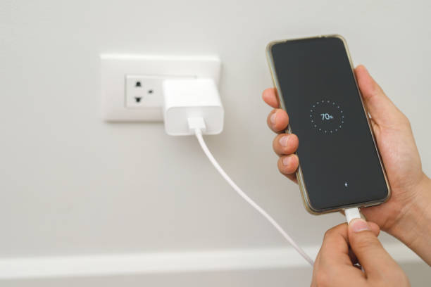 istock close up hand plugging adapter charge the battery with outlet socket plug and hold mobile phone on wall ,electric safety concept 1475038352