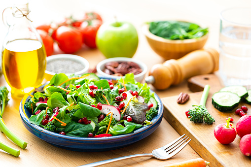 Healthy eating: fresh salad plate shot on wooden table. Ingredients like carrots, radish, broccoli, spinach, pecan, chia seeds and olive oil complete the composition. High resolution 42Mp studio digital capture taken with Sony A7rII and Sony FE 90mm f2.8 macro G OSS lens