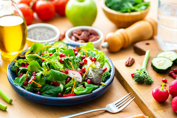 Healthy eating: fresh salad plate shot on wooden table. Ingredients like carrots, radish, broccoli, spinach, pecan, chia seeds and olive oil complete the composition. High resolution 42Mp studio digital capture taken with Sony A7rII and Sony FE 90mm f2.8 macro G OSS lens