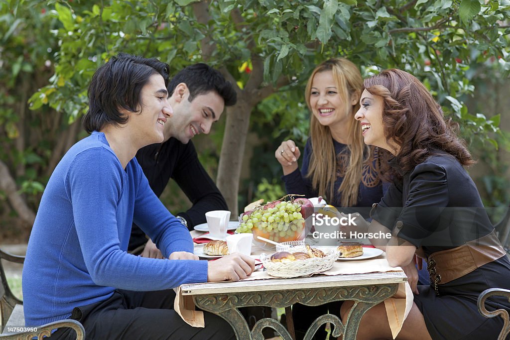 Young Friends Enjoying Coffee At A Restaurant A group of four young friends enjoy a healthy snack and coffie at an outdoor restaurant Coffee - Drink Stock Photo