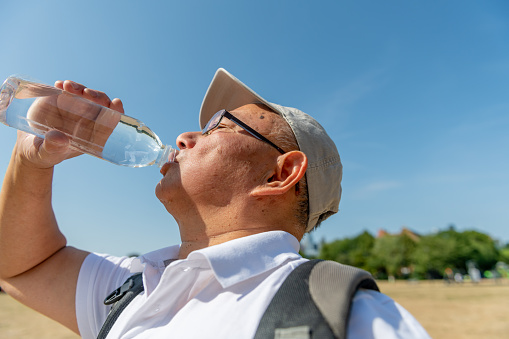 A senior man drinking plenty of water on a record breaking hot summer day to avoid dehydration while out and about.