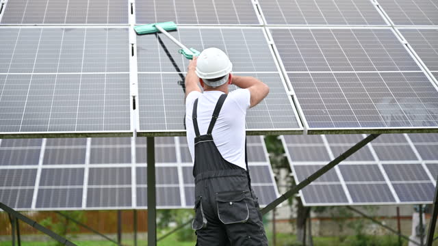 Male worker cleaning solar battery by mop.