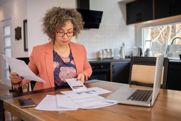 istock Mature woman using calculator while going through bills and home finances 1475042324