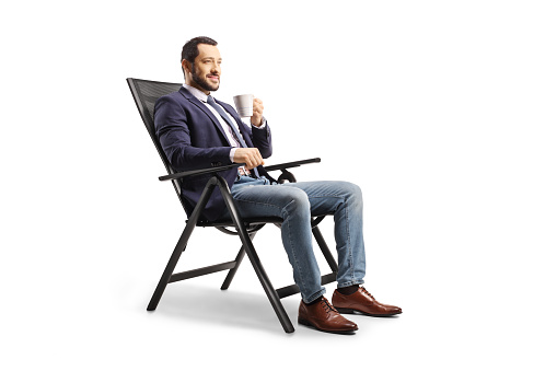 Young man resting in a foldable chair and holding a cup isolated on white background