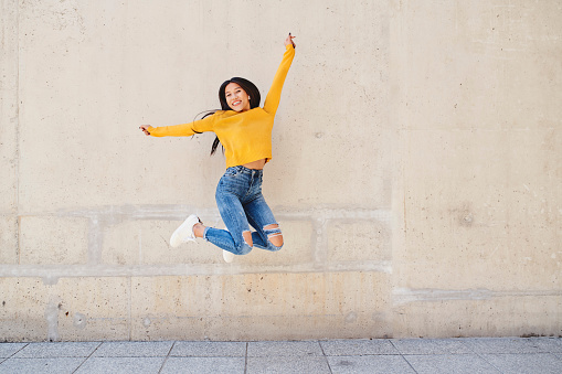 Happy asian woman jumping against concrete wall in the city