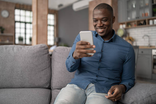 istock Excited Black African American Man Using Smartphone for mobile shopping while Sitting on the Sofa in Living Room. Happy Man buying things, shopping online 1475044081