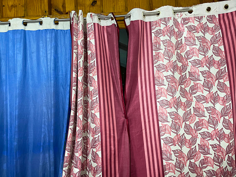 Stock photo showing close-up view of cheap, mismatched block blue and pink, leaf patterned eyelet curtains in wooden beach house.