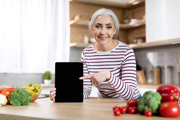 istock Smiling Elderly Lady Pointing At Blank Digital Tablet Screen In Kitchen, Mockup 1475047749