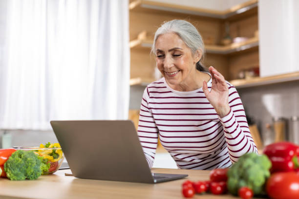 istock Smiling Senior Woman Making Video Call With Laptop While Resting In Kitchen 1475048877