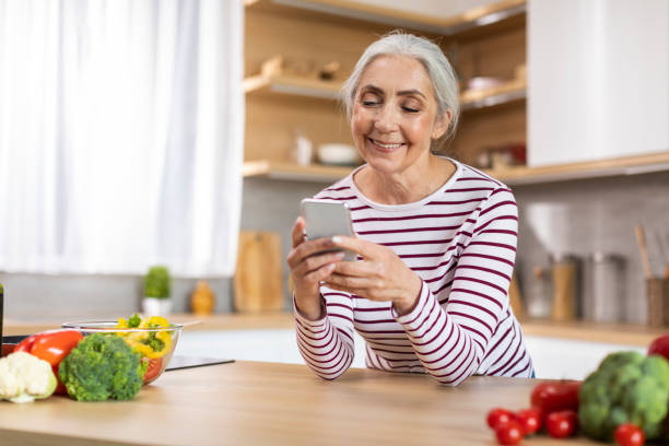istock Mobile Communication. Portrait Of Smiling Senior Lady Using Smartphone In Kitchen Interior 1475048881