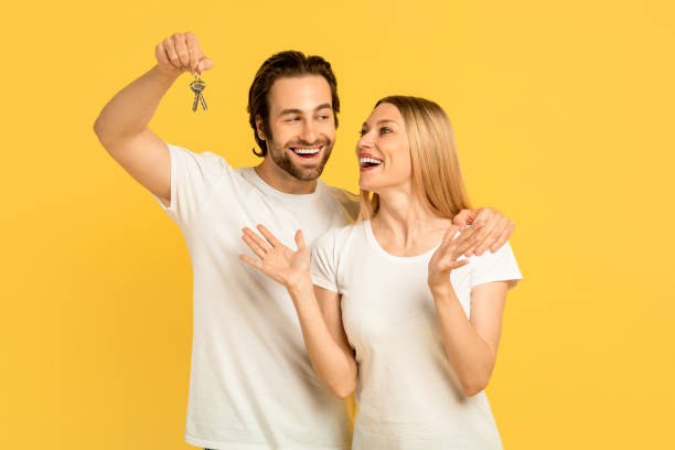 幸せな幸せなミレニアル世代の白人男性は、白いtシャツを着た興奮した女性に鍵を見せる - residential home 写真 ストックフォトと画像