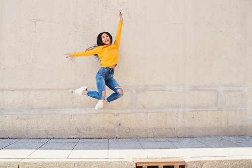 Happy asian woman jumping against conrete wall in the city