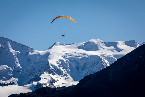 Extreme sports. Action shot of a speed flyer zooming past, high above a mountain peak towards the sun.