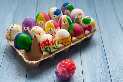 The hands of a little caucasian girl show the end result of a homemade felt easter egg, sitting at a children's table with a set of crafts on a pink background with depth of field, close-up side view. The concept of crafts, diy, needlework, diy, children art, artisanal, Easter preparation, children creative.