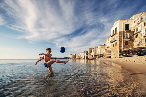 adolescente jugando con pelota en la playa en una pequeña ciudad siciliana - beach football fotografías e imágenes de stock
