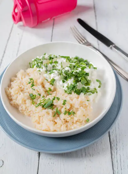Homemade easy and simple fitness dinner or lunch with brown rice, cottage cheese and chive. Low fat, gluten free and high protein. Served ready to eat on a plate isolated on white background.