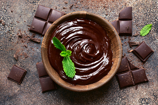 Homemade mint chocolate ganache in a wooden bowl on a dark slate, stone or concrete background. Top view with copy space.