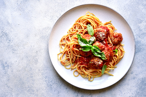 Pasta spaghetti with meat ball in tomato sauce on a plate over light grey slate, stone or concrete background. Top view with copy space.