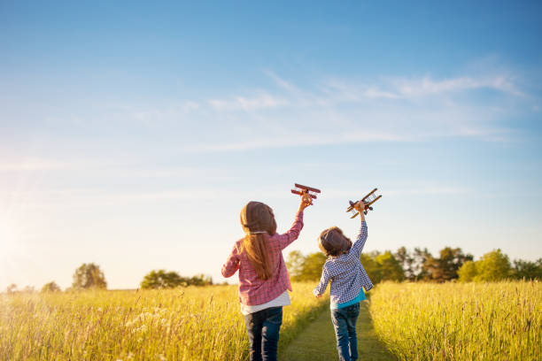 garçon et fille jouant avec des avions en bois sur le terrain au coucher du soleil - aspirations pilot child airplane photos et images de collection