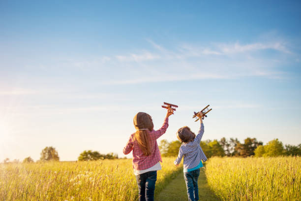 мальчик и девочка играют с деревянными плоскостями на поле на закате - aspirations pilot child airplane стоковые фото и изображения