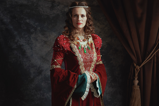 medieval queen in red dress on dark gray background.