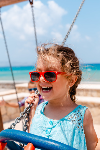 Sweet little girl swinging on a swing on public beach