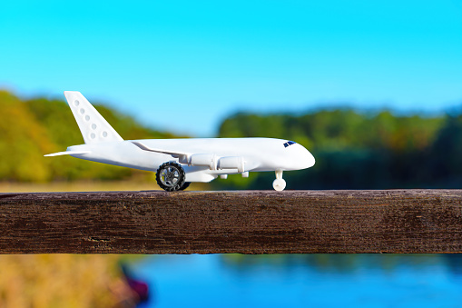 Toy plane model resting on a wooden railing against a stunning natural landscape of water and trees. Visual for designs related to childhood, imagination and the joy of exploration.